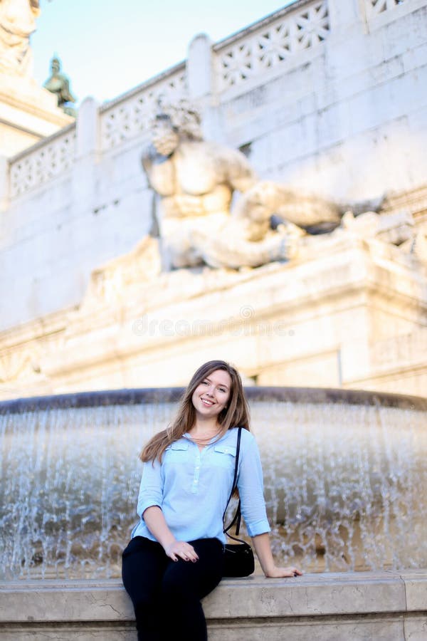 Chica joven que se sienta cerca de la fuente del Trevi, camisa azul que lleva fotografía de archivo libre de regalías Chica joven que se sienta cerca de la fuente del Trevi, camisa azul que lleva fotografía de archivo libre de regalías