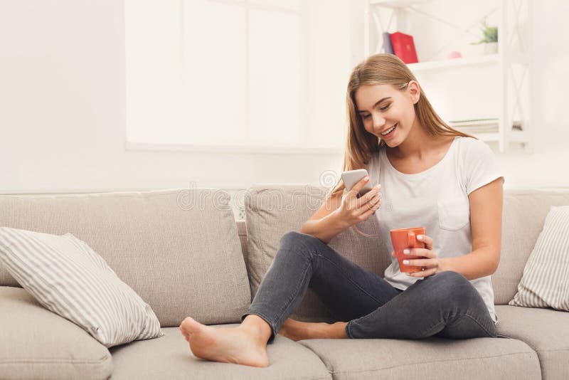 Chica joven que usa el teléfono móvil en el sofá foto de archivo libre de regalías Chica joven que usa el teléfono móvil en el sofá foto de archivo libre de regalías
