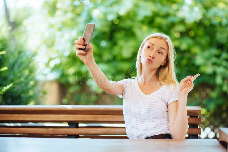 Chica joven sonriente que hace la foto del selfie en smartphone fotografía de archivo Chica joven sonriente que hace la foto del selfie en smartphone fotografía de archivo