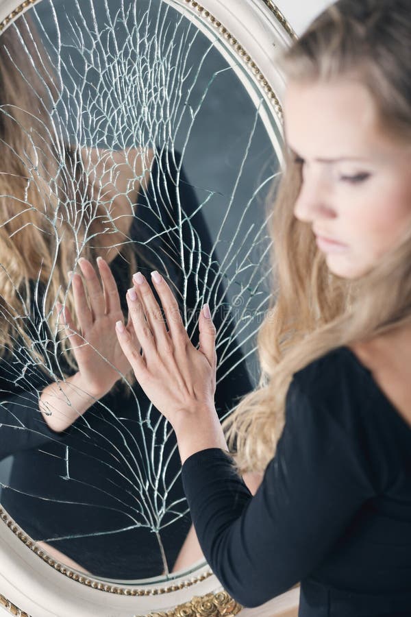 Depressed young girl with mental illness standing in front of broken mirror. Depressed young girl with mental illness standing in front of broken mirror