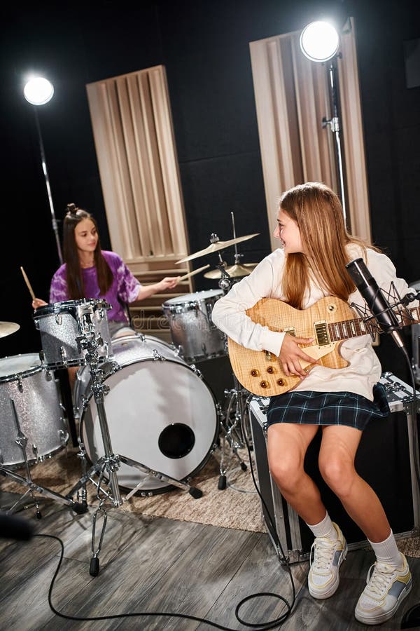 pretty blonde teenage girl with guitar looking at her brunette friend playing drums in studio, stock photo. pretty blonde teenage girl with guitar looking at her brunette friend playing drums in studio, stock photo