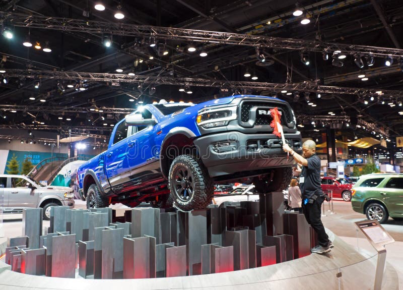 CHICAGO, ILLINOIS - February 8, 2020: Male person dusting an elevated blue RAM pickup truck displayed at McCormick Place at the annual Chicago Auto Show. CHICAGO, ILLINOIS - February 8, 2020: Male person dusting an elevated blue RAM pickup truck displayed at McCormick Place at the annual Chicago Auto Show