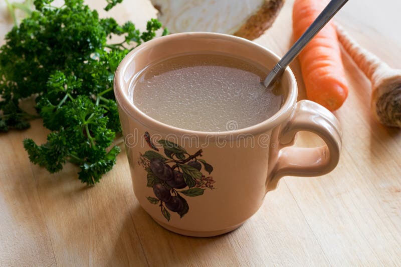 Chicken Bone Broth in a Mug with Vegetables in the Background Stock