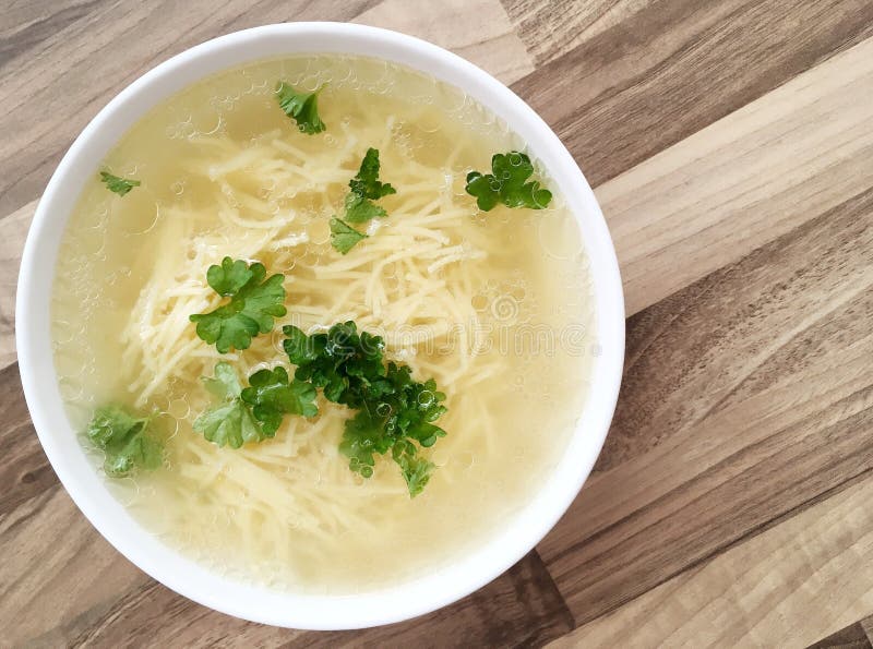 Rich chicken bouillon with noodles and parsley. Top view. Wooden background. Rich chicken bouillon with noodles and parsley. Top view. Wooden background.