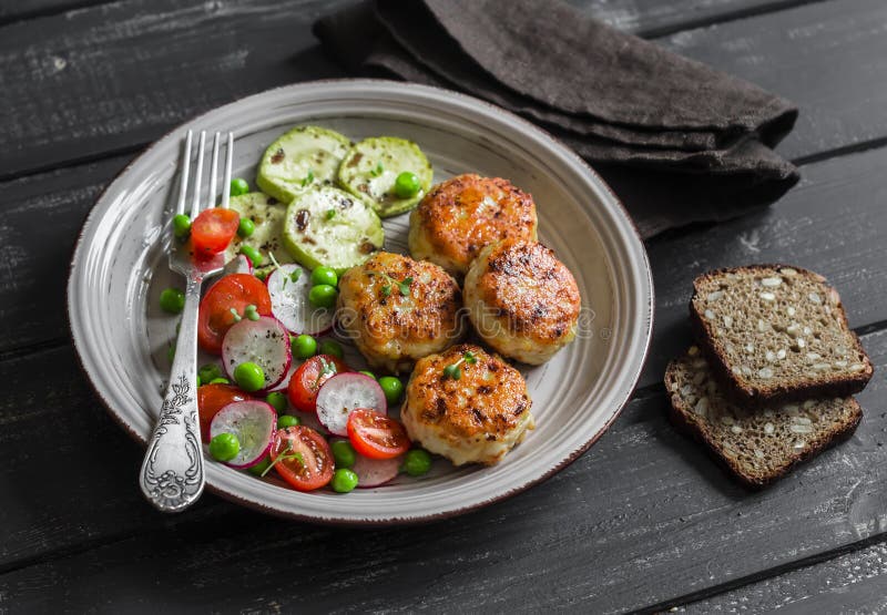 Chicken cutlets and fresh vegetable salad on ceramic plate on dark wooden background. Healthy and tasty food