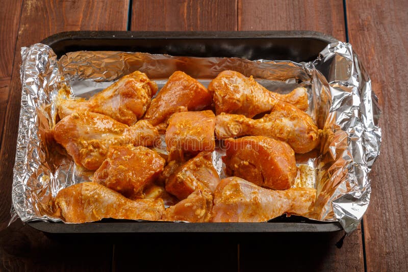 Chicken Drumsticks in Soy Sauce and Spices Marinated on Foil on a Baking Sheet on a Wooden Table