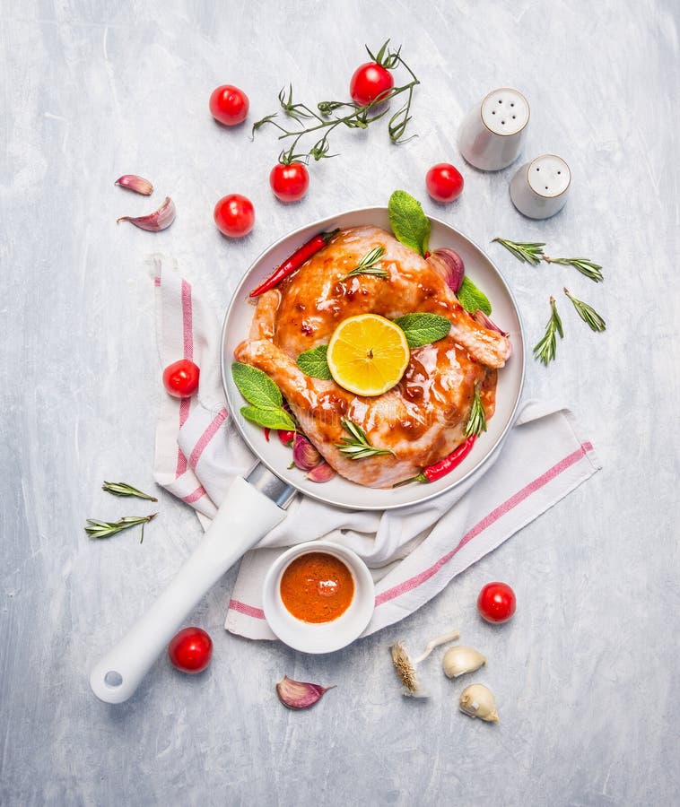 Chicken legs with red chili marinade, herbs and spices in white pan on blue wooden background