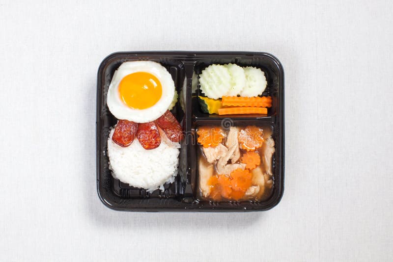 Chicken with sauce with fried egg on rice put in a black plastic box, put on a white tablecloth, food box