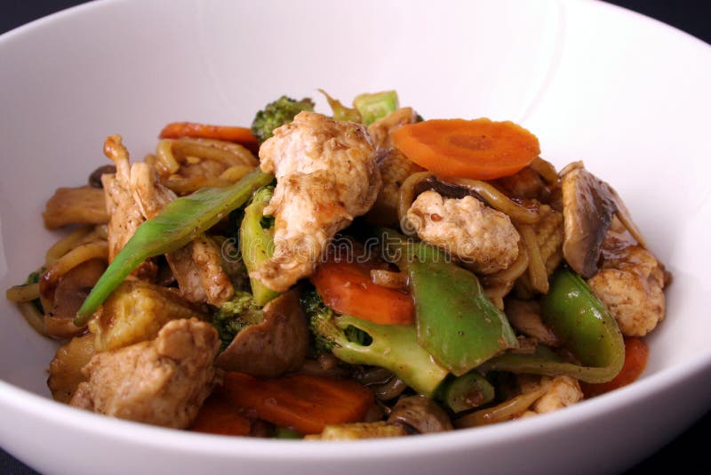 A freshly cooked chicken stir fry with fresh vegetables and singapore noodles served in a white bowl