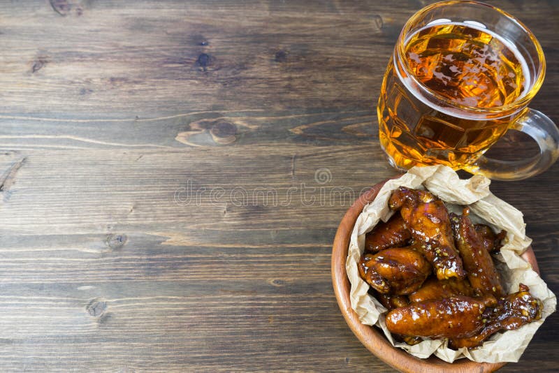 Chicken wings in a fragrant and pungent sauce with sesame seeds. A glass of fresh cold beer and fried potatoes with rustic tomato