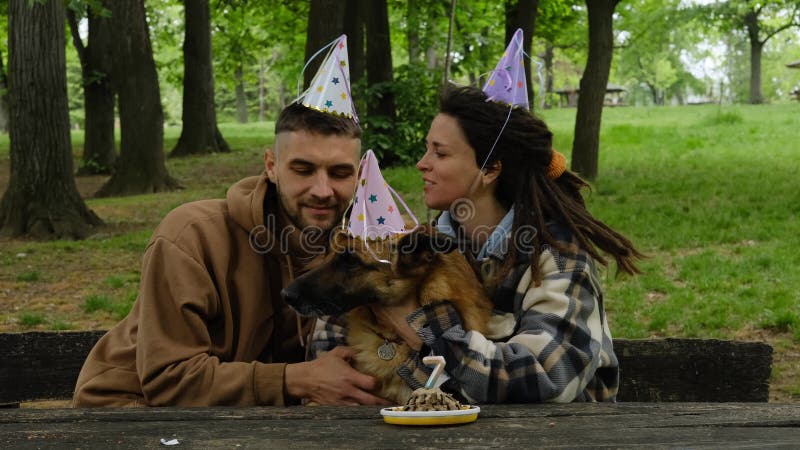 Chien fête l'anniversaire en famille. jeune couple embrasse berger allemand des deux côtés dans le parc vert de printemps. chien