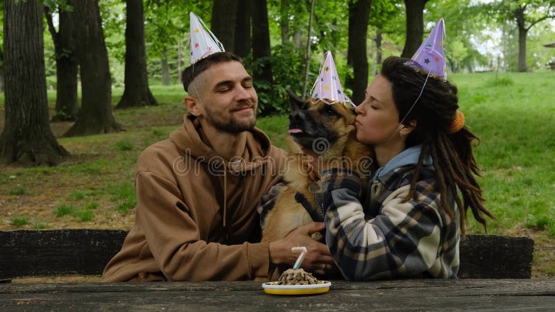 Chien fête l'anniversaire en famille. jeune couple embrasse berger allemand des deux côtés dans le parc vert de printemps. chien