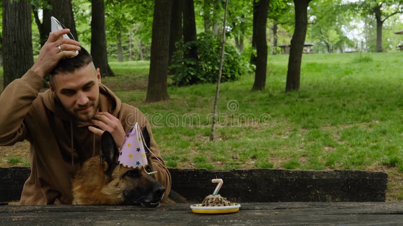 Chien fête son anniversaire avec un propriétaire mâle à l'extérieur. jeune homme embrasse berger allemand dans le parc vert du pri
