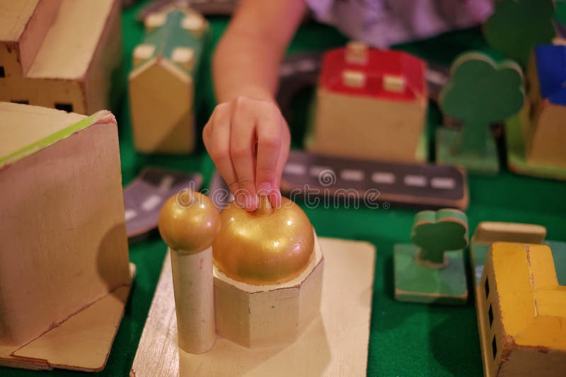 A child adding a wooden mosque block to her modeled city with road, buildings and trees stock photos