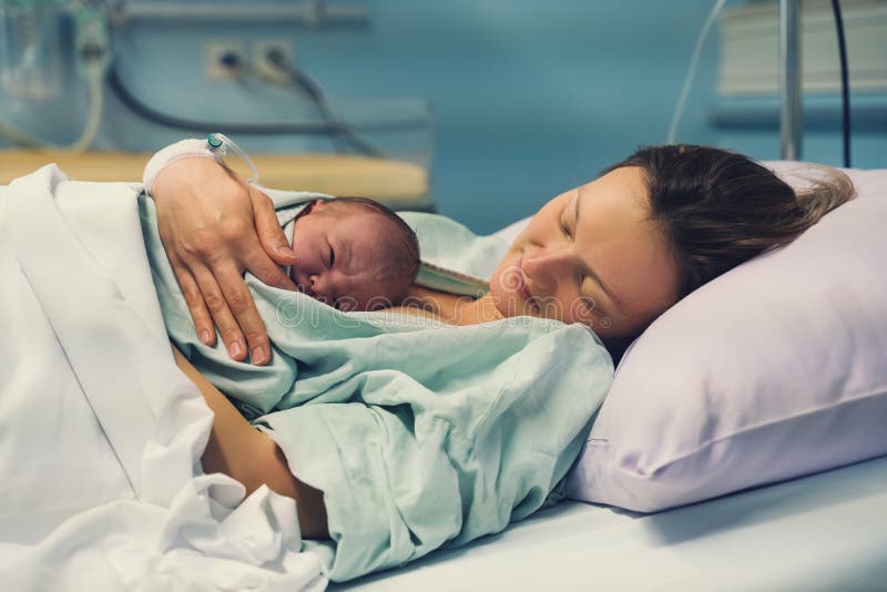 Child birth in maternity hospital. Mother and newborn. Young mom hugging her newborn baby after delivery. Woman giving birth