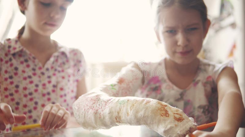 Child draws on plaster. The girl paints a plastered hand to her sister. Girlfriend cares about a sick friend.