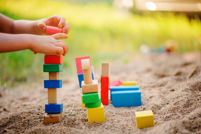 Child building toy houses of colorful wooden bricks in sandbox