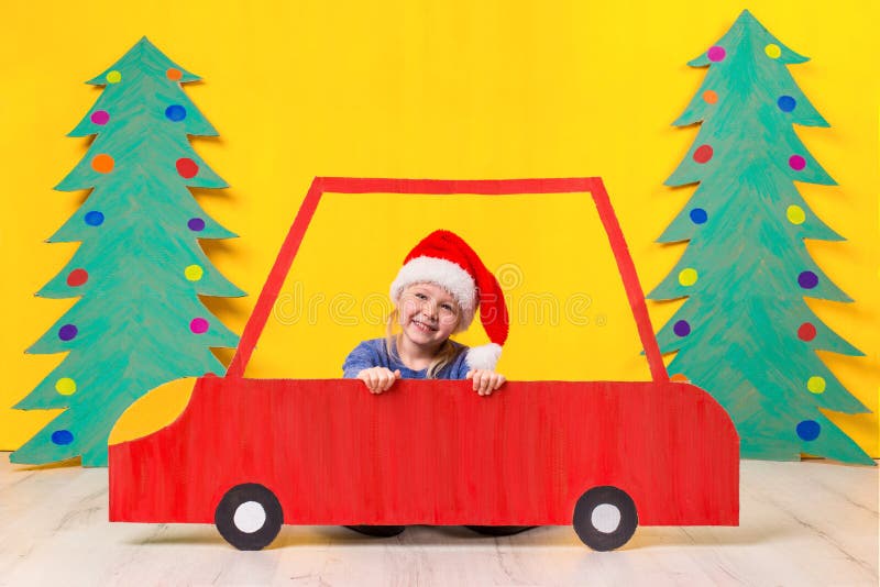 Child with Christmas hat driving a car made of cardboard. Christmas concept. New Year`s holidays.