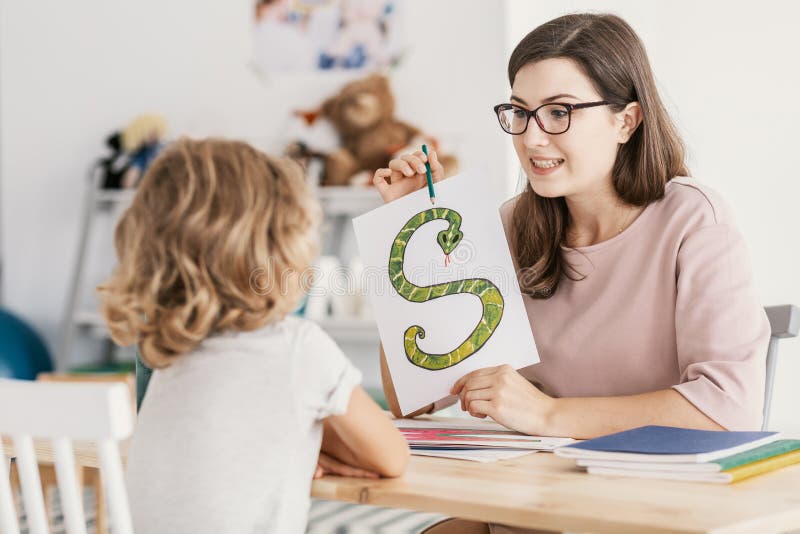 A child with development problems with a professional speech therapist during a meeting. Tutor holding a prop poster of a snake as