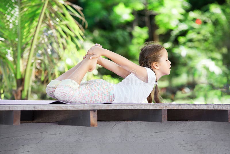 Child doing exercise on platform outdoors. Healthy lifestyle. Yoga girl