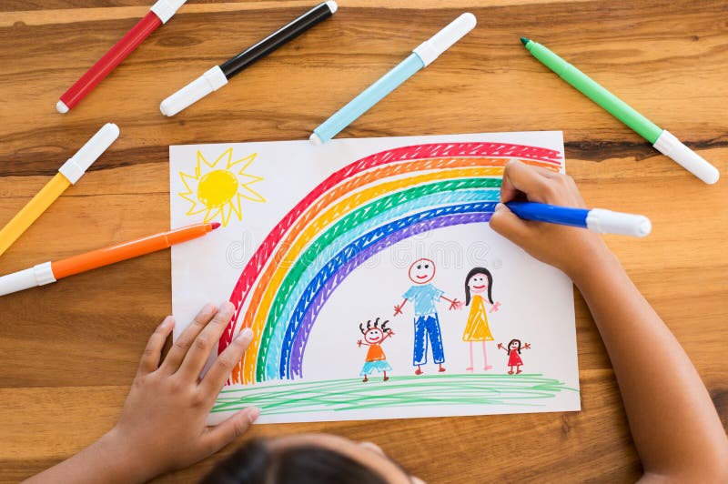 Top view of little girlâ€™s hands painting happy family with marker on white paper. Drawing sheet with artwork by daughter on table. Little girl using marker to make family painting with rainbow. Top view of little girlâ€™s hands painting happy family with marker on white paper. Drawing sheet with artwork by daughter on table. Little girl using marker to make family painting with rainbow.