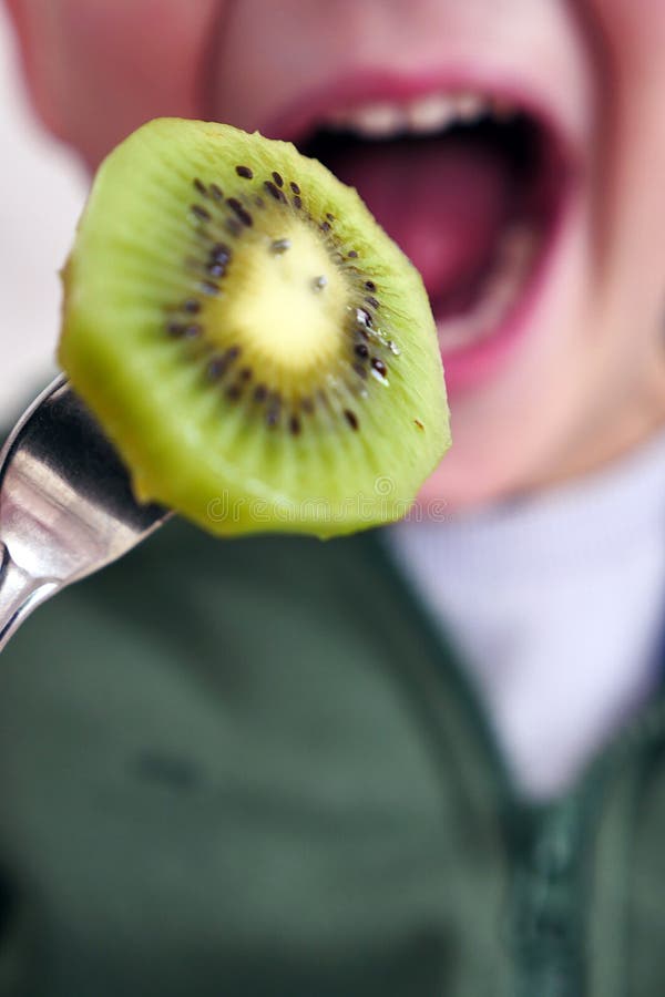 A Child Eating a Kiwi with His Mouth Open, a Slice of Kiwi Fruit Stuck