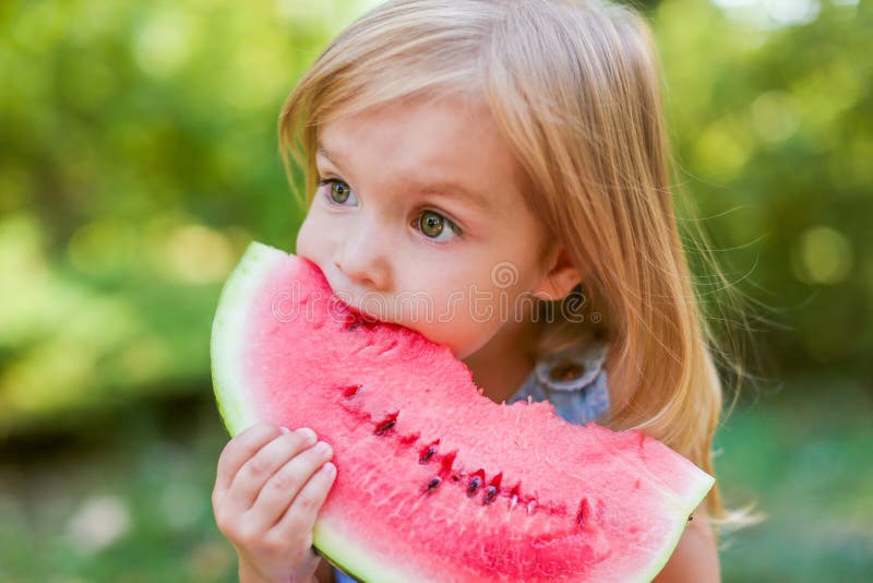 Child eating watermelon in the garden. Kids eat fruit outdoors. Healthy snack for children. 2 years old girl enjoying watermelon