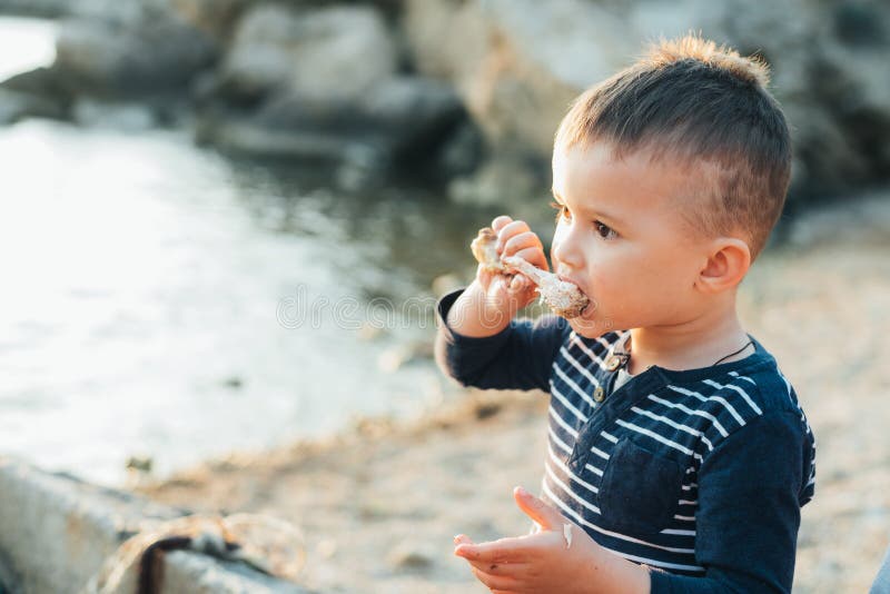 The Child Eats a Chicken Drumstick Cooked on the BBQ Stock Photo