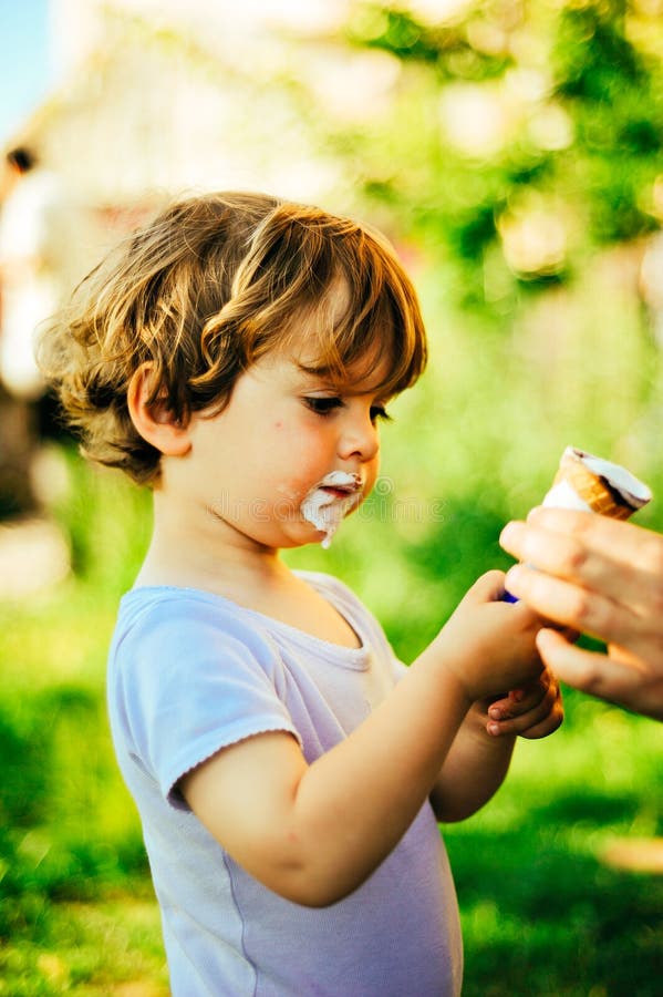 Child eats ice cream on a summer day in the shade of a tree