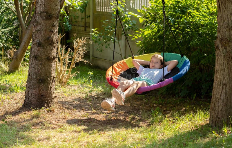 Child, elementary school age girl relaxing on an outdoor swing, laying in the sun, taking a break, one person, real people lifestyle, copy space. Leisure and recreation concept, boredom, rest