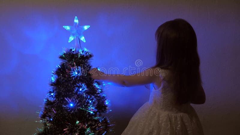 Child examines a christmas star on a holiday tree. little girl plays near a Christmas tree in a children`s room