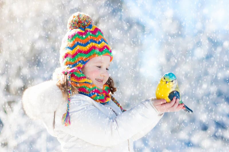 Child feeding bird in winter park. Kids play in snow. Nature and