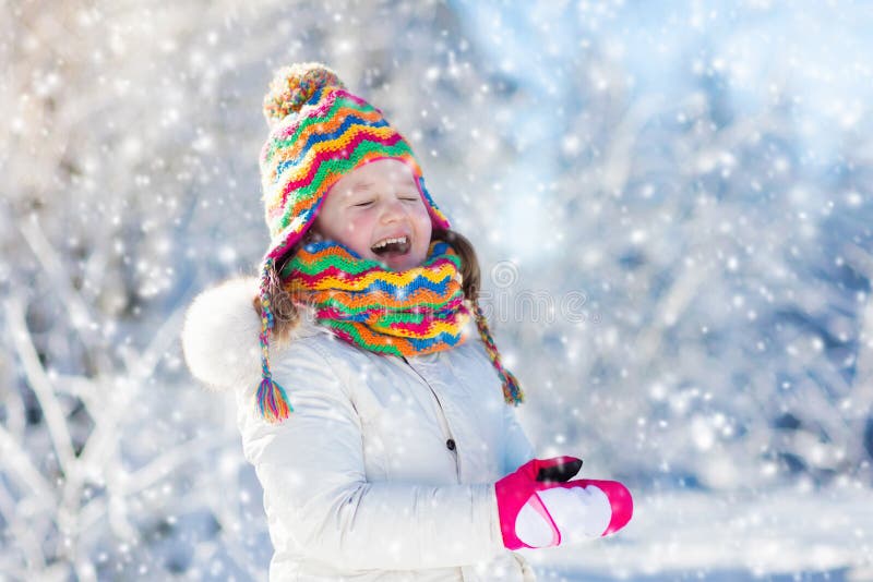 Child feeding bird in winter park. Kids play in snow. Nature and