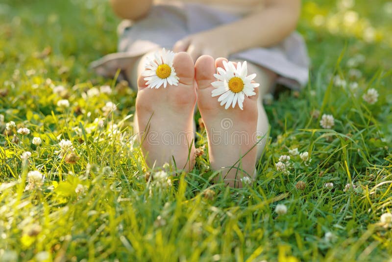 Child feet with daisy flower on green grass