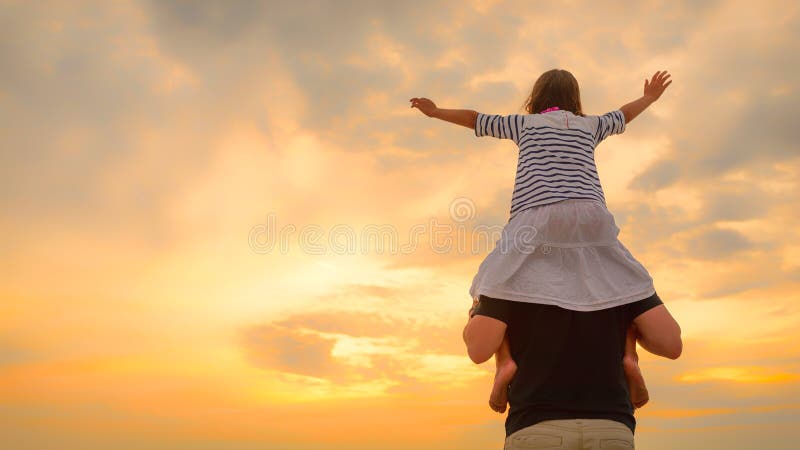 Child girl on dad`s shoulders on the background of the setting sun on a beach stock photo Child girl on dad`s shoulders on the background of the setting sun on a beach stock photo