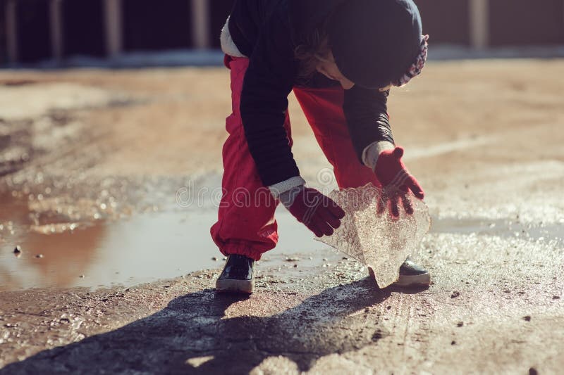 Child girl exploring nature and playing with block of ice outdoor on early spring walk