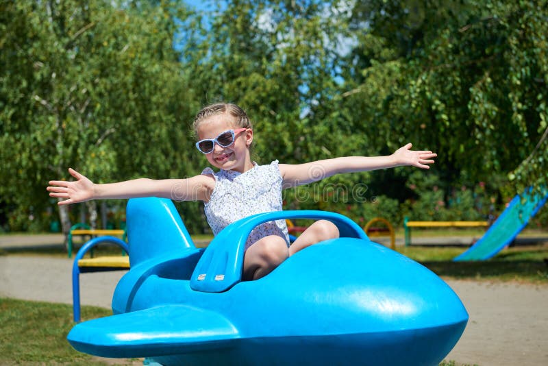 Child girl fly on blue plane attraction in city park, happy childhood, summer vacation concept