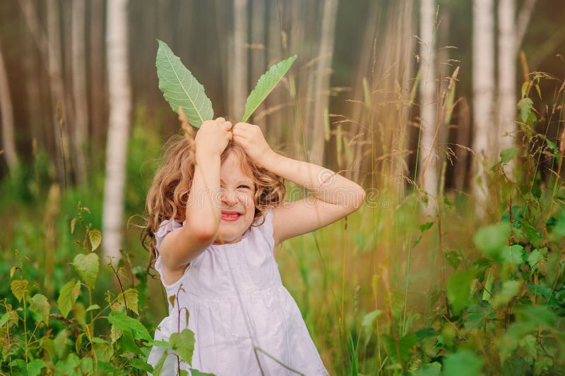 Child girl playing with leaves in summer forest with birch trees. Nature exploration with kids.