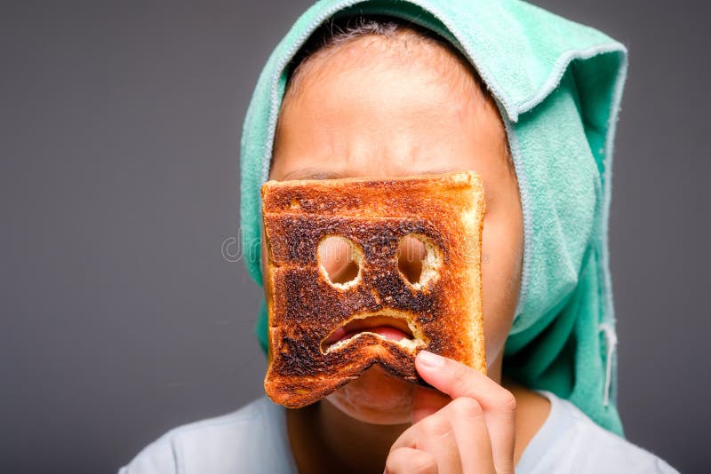 Child girl with towel on her head after bath show the scared icon face on the burnt toast, funny moment of mistake, danger of charred food concept. Child girl with towel on her head after bath show the scared icon face on the burnt toast, funny moment of mistake, danger of charred food concept