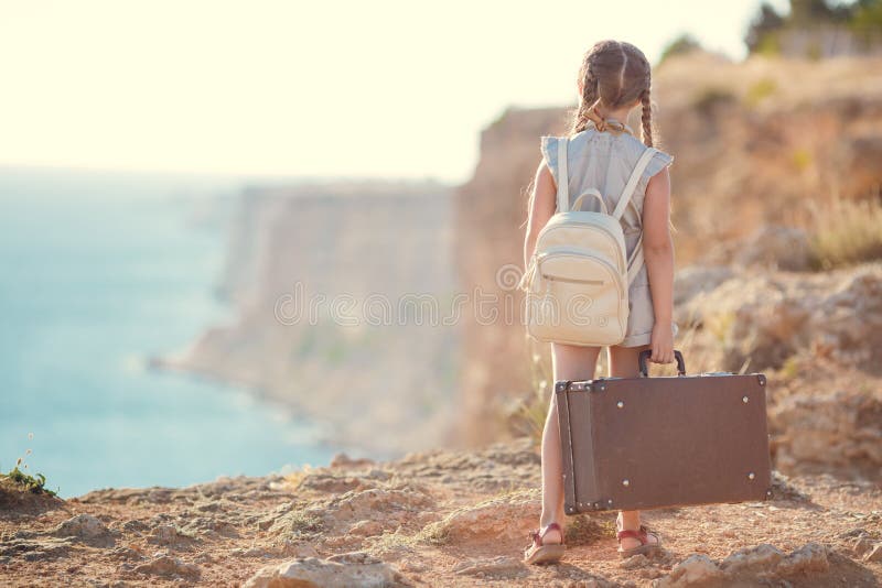Child girl traveler. trip alone. girl walking with camera and suitcase on nature by sea. travel, vacation, holidays. High quality photo