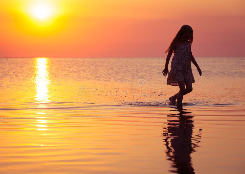 Child girl walking at the sunset sea
