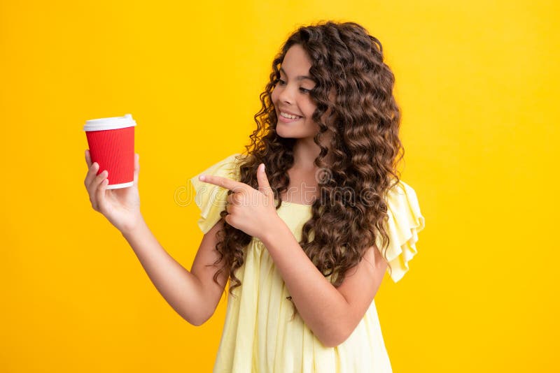 Child girl 12, 13, 14 years old with take away cup of cappuccino coffee or tea. Teenager with takeaway mug on yellow