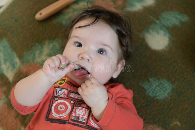 Child gnaws a bone. One-year-old baby gnaws a plastic toy because his teething. Little cheerful boy in a light green suit with royalty free stock photo Child gnaws a bone. One-year-old baby gnaws a plastic toy because his teething. Little cheerful boy in a light green suit with royalty free stock photo