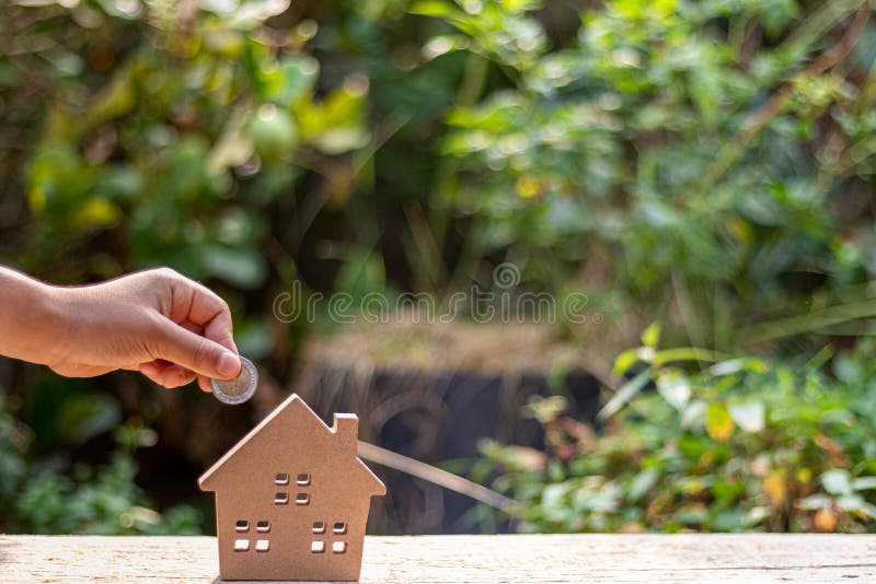 Child hand putting a coin into small wooden toy house with natural green blur background. stock photography Child hand putting a coin into small wooden toy house with natural green blur background. stock photography