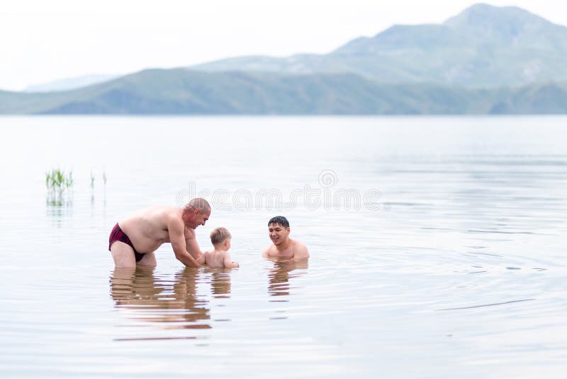Child with his grandfather and father play and swin in sea, summer time