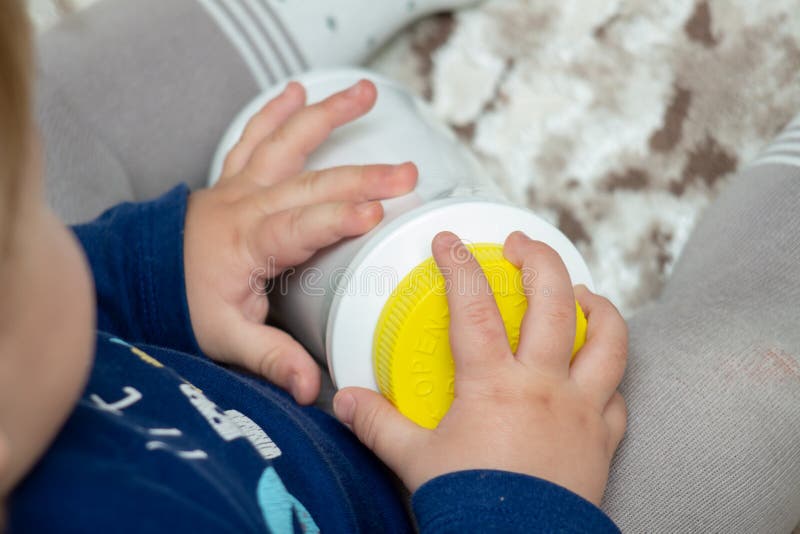 A child independently tries to open a plastic bottle of medicine, close-up. Child-resistant, childproof or CR packaging. Push&Turn