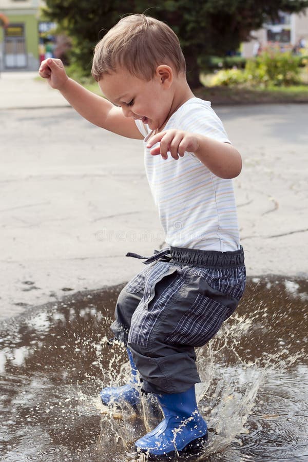 Happy child jumping into a street puddle. Happy child jumping into a street puddle.