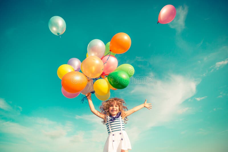 child jumping with toy balloons in spring field happy colorful outdoors smiling kid having fun green against blue sky background