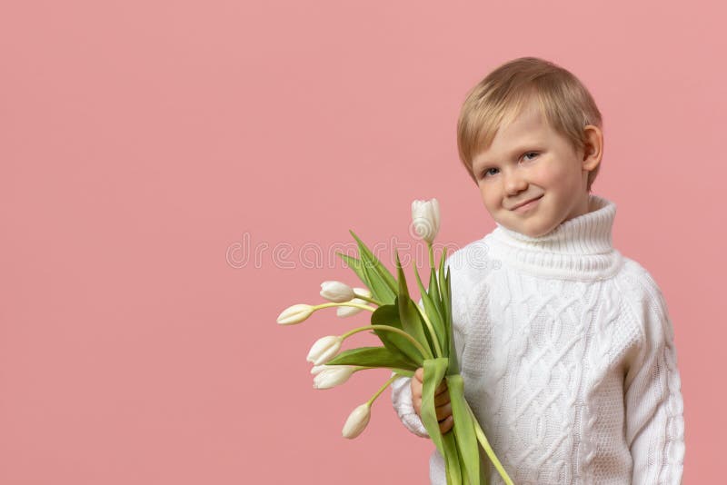 Child kid boy with flowers white tulips in knitted sweater on pink solid background with copy space. Concept for Valentine day