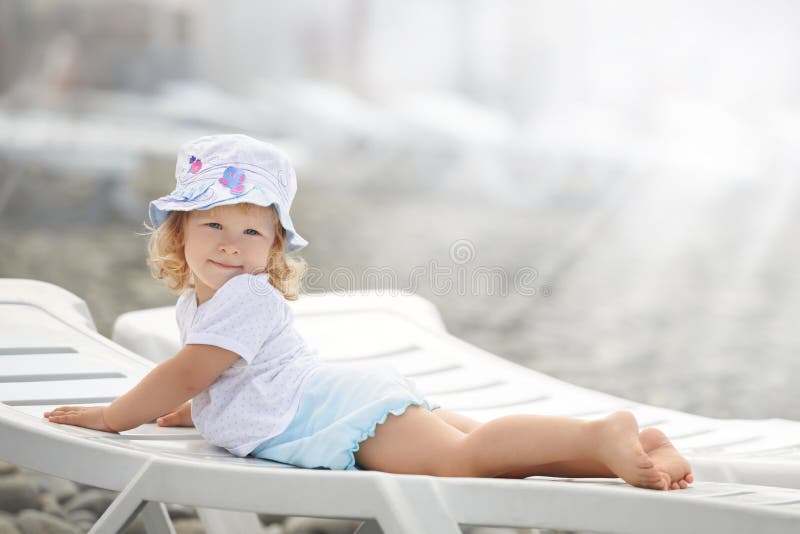 Bambino posa sulla spiaggia chaise long alla luce del sole.